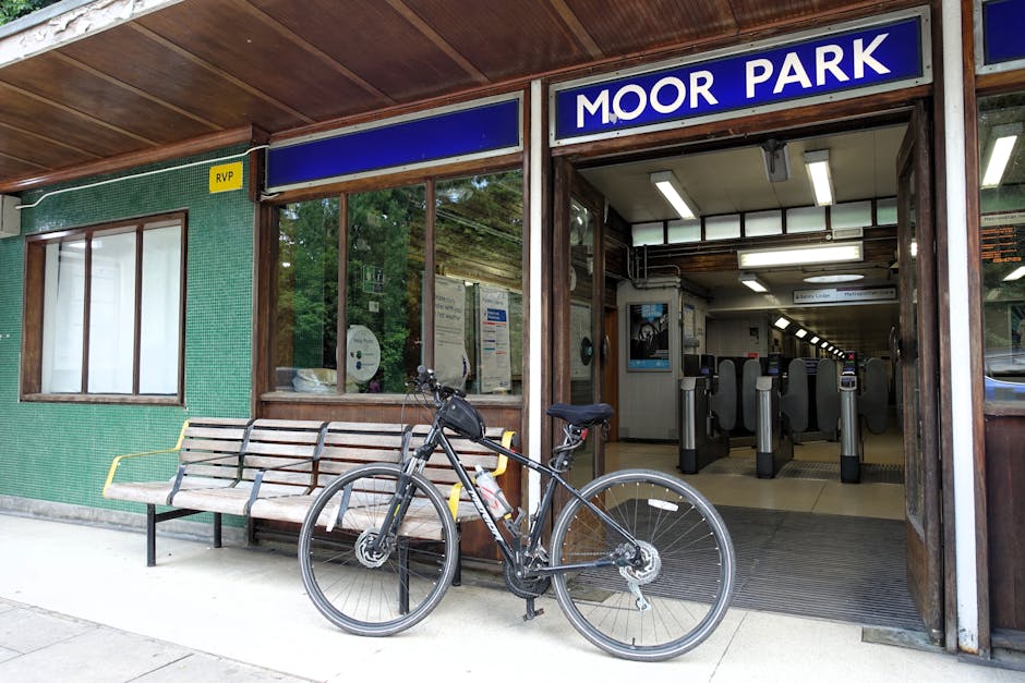 The exterior of Moor Park station entrance, featuring a blue sign with white text, is shown with a wooden and glass façade. A wooden bench with metal armrests is positioned outside the station, next 