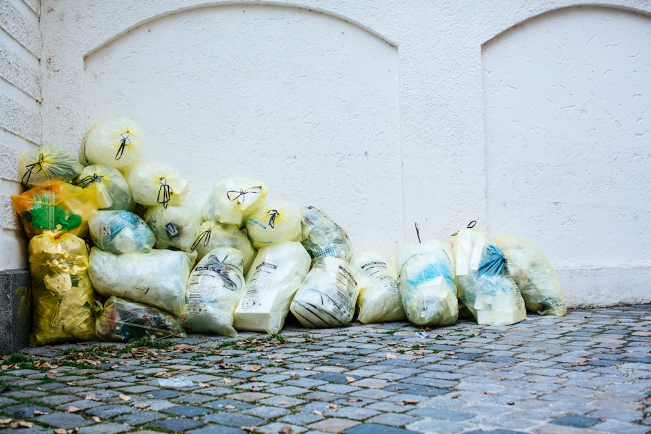 A row of eight large black plastic wheelie bins with orange and blue lid tops, arranged outside against a red brick wall, likely used for waste disposal and recycling during a house move or furniture 